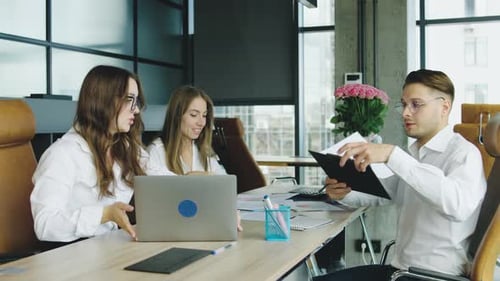 Three Professionals Collaborate at a Modern Office Workspace Reviewing Documents and Discussing