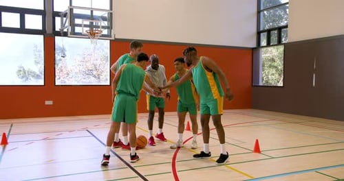 Basketball players practicing dribbling skills with coach in indoor gym