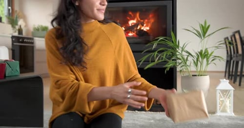 Woman Wrapping Christmas Gifts by Cozy Fireplace