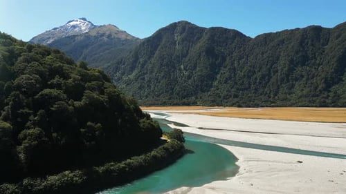 Aerial drone shot of clear green narrow river surrounded by mountain range covered with green vegeta