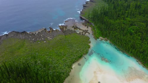 Drone shot of a separation between a natural pool with a beach and the ocean crashing is waves on th