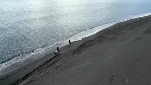 Luftaufnahmen von Reitern an einem leeren schwarzen Sandstrand