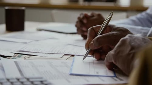 Black Senior Man Writing Checks and Paying Bills with Young Woman Helping