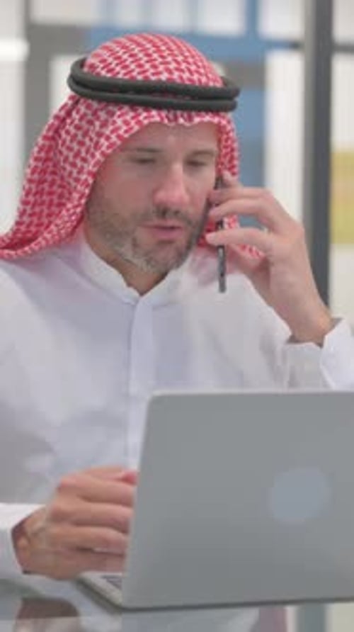 Arab Businessman Working on Laptop and Talking on Phone