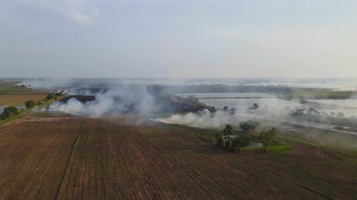 Descending aerial footage revealing a newly tilled field and smoke rising from burning grass, Grassl
