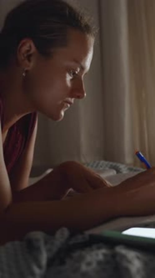 Woman Writes in Notebook at Night on Bed