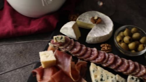 Fondue pot (caquelon) with melted cheese and snacks on gray table. Camera moving left and up