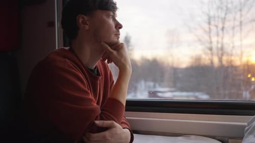A Young Man Travels in a Train Looks Thoughtfully Out the Window During Sunset