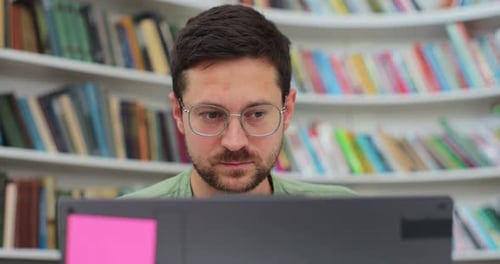 Man Student Preparing Exam and Learning Lessons in Library Making Research on Laptop and Browse
