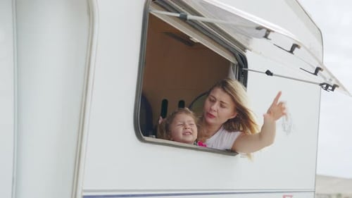 Cheerful Mother and Daughter Look Out of the Camper Window at Nature Family Holidays