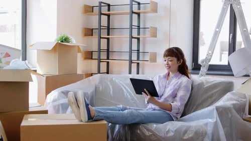 Woman Relaxes in New Home with Tablet Surrounded by Boxes