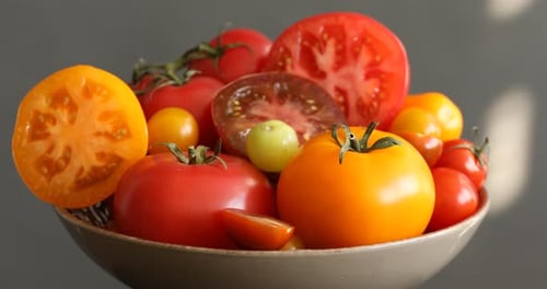 Verschiedene reife Tomaten in Schale vor grauem Hintergrund, rotierend