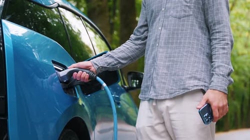 Young man charging electric car outdoor at green forest. Save ecology alternative energy sustainable