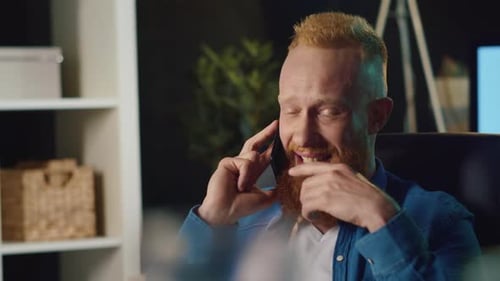 Smiling man with beard talking on phone indoors