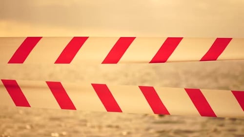 Red White Warning Tape Barrier Ribbon Swinging in the Wind Across Exotic Sea Beach Background