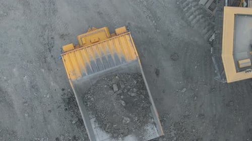 Mine excavator loading coal into an open pit dump truck, drone view.