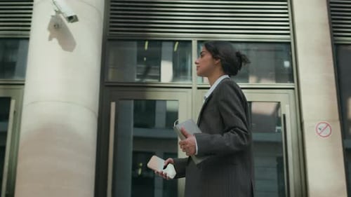 Female CEO in Formal Business Suit Walking Past Modern Glass-Fronted Building