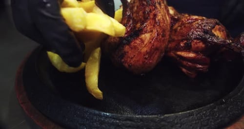 Amazing slow motion zoom in shot of a plate of roast chicken with fries as a chef wearing black glov