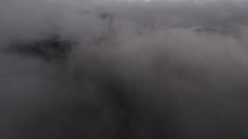 Aerial drone footage of a foggy day on top of clouds, revealing a mountain and sun coming trough the