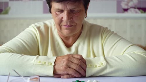 Senior Woman with Pills and Eyeglasses on Table