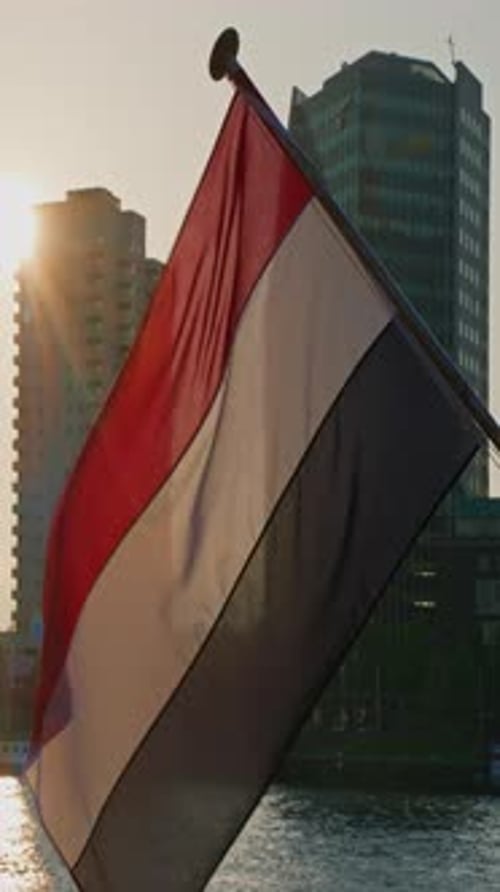 Vertical Video Real Large Netherlands Flag Waving in De Wind at the Cityscape at Sunset The Dutch