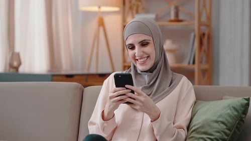 Smiling Woman Using Smartphone on Couch Indoors