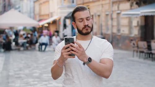 Handsome Man Uses Phone on Cobblestone Street