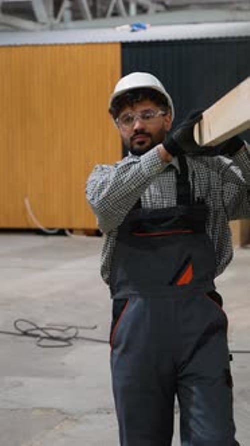 Construction Worker Carrying Wooden Plank in Factory