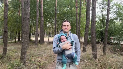 Young Father with His Newborn Baby in a Sling Walking in the Autumn Forest The Concept of a Happy