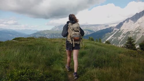 view from behind of a hiker tourist traveler woman with backpack trekking and walking on a mountain