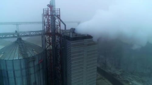Grain processing plant premises on gray foggy day.