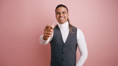 Smiling Young Man Holding an Invisible Dental Aligner