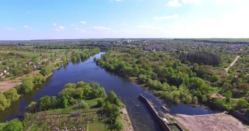 Bridge and dam over the narrow river. Drone footage over the river flowing between picturesque banks