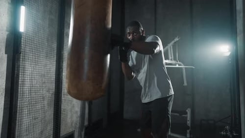 Boxer Training Hitting Punching Bag African American Sweated Sportsman Practicing Punches in Gym