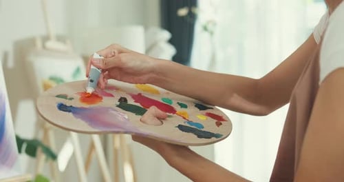 Frauen tragen eine Schürze mit einer Palette von Farben. Verwenden Sie Pinsel, malen Sie auf Leinwand und kreieren Sie Kunstwerke in der Werkstatt.