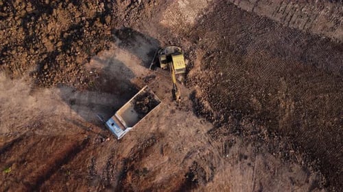 Aerial view of a wheel loader excavator with a backhoe loading sand into a heavy earthmover