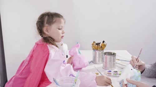 Kleines Mädchen bemalt Pappmaché-Figuren mit Acrylfarbe für ihr Homeschooling-Kunstprojekt