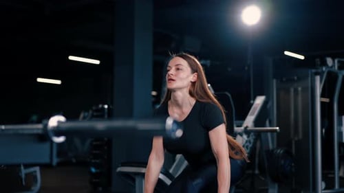 concentrated fitness woman trainer doing exercises with dumbbells in hands pumping muscles in gym