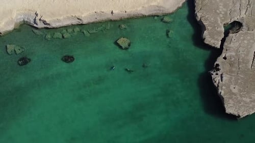 Two people diving on the turquoise water of patagonian sea, revealing a beautiful landscape - Aerial