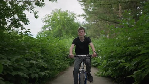 Young Boy Smiling While Cycling on Scenic Path Surrounded By Lush Greenery