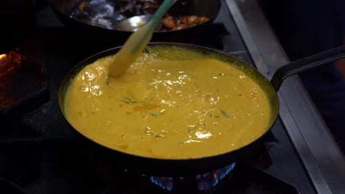 Chef using a spatula stirring the delicious yellow curry with fresh curry leaves in hot boiling pan,