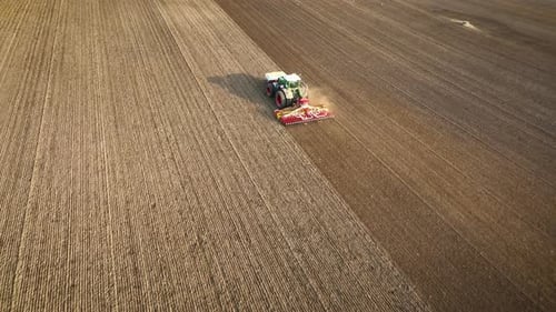 Aerial footage of tractor sowing seeds in even rows across a vast, freshly plowed field, showcasing