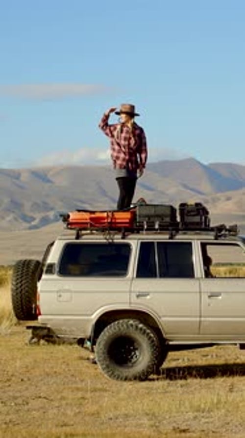 Traveler Standing Atop SUV in Rural Landscape