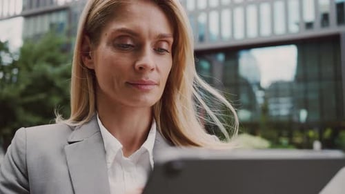 Attractive Woman Typing on Tablet Near Office Building