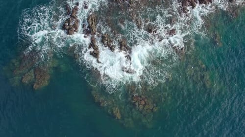 Top Down Drone View of Ocean Waves Crashing on Jagged Rocks