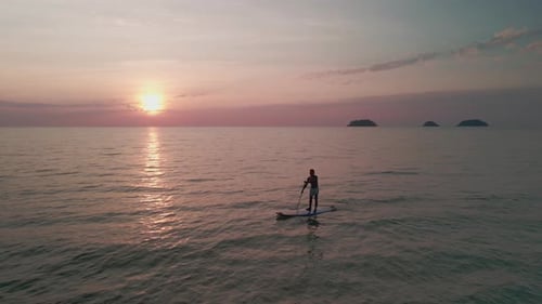 aerial shot of stand up paddle boarder paddling in ocean at sunset with islands in distance