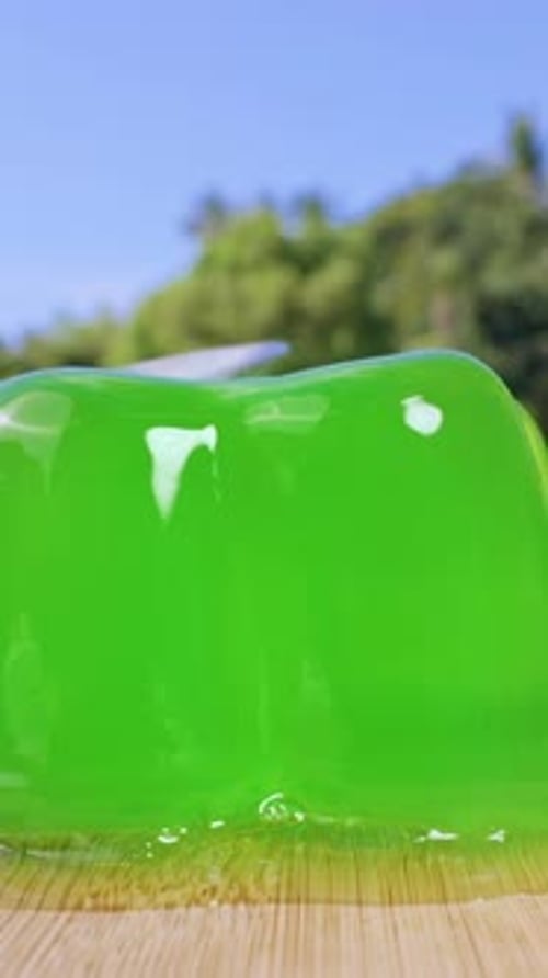 Vertical video. Close Up Shot of Green Jelly on Wooden Board Wobbling After Spoon Touch, Slow Motion