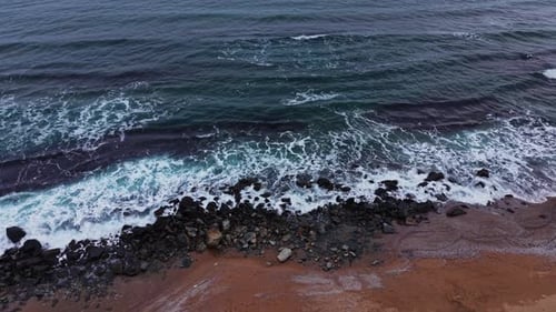 Waves crash on rocks at shoreline near sandy beach during daytime