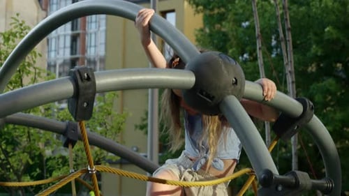 Young Girl Climbs Playground Structure in Urban Park During Sunny Afternoon