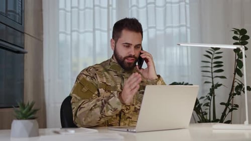 Man Typing on Laptop While Talking on Phone